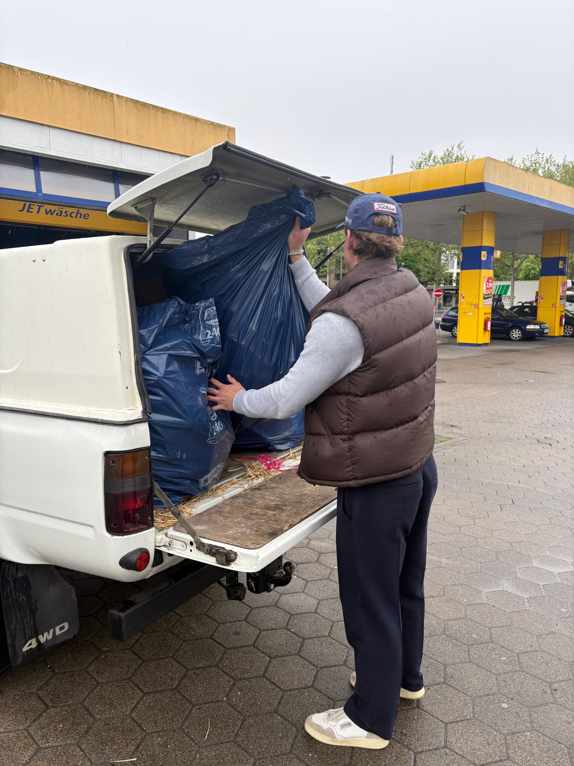 Zu sehen ist ein Schüler, der aus dem Kofferraum des Autos Pfandsäcke nimmt, um diese abzugeben