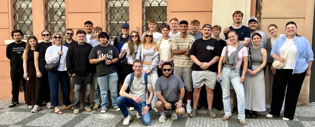 Zu sehen ist eine Schulklasse in Prag vor einem Gebäude. Die Personen lächeln in die Kamera