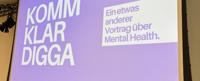 Große Leinwand in einer Aula mit einer lila Präsentationsfolie. Darauf steht links „Komm klar Digga“ und rechts „Ein etwas anderer Vortrag über Mental Health.“